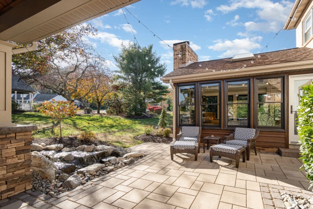 A beautiful patio with an enclosed porch behind a house.
